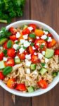 a colorful rotisserie chicken bowl with quinoa, vegetables, and feta cheese on a rustic table.
